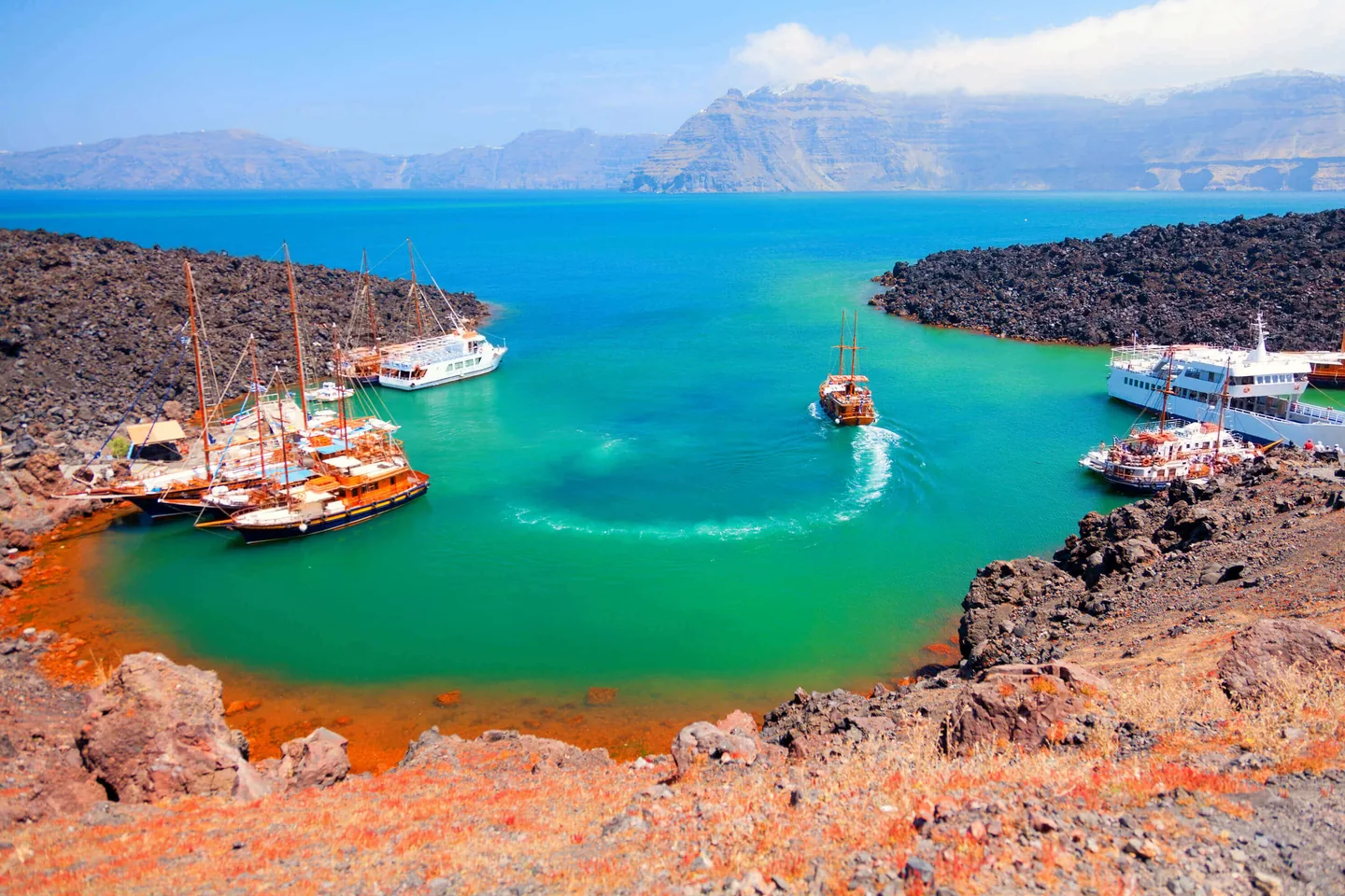Excursion boats and turquoise volcanic cove framed by caldera cliffs